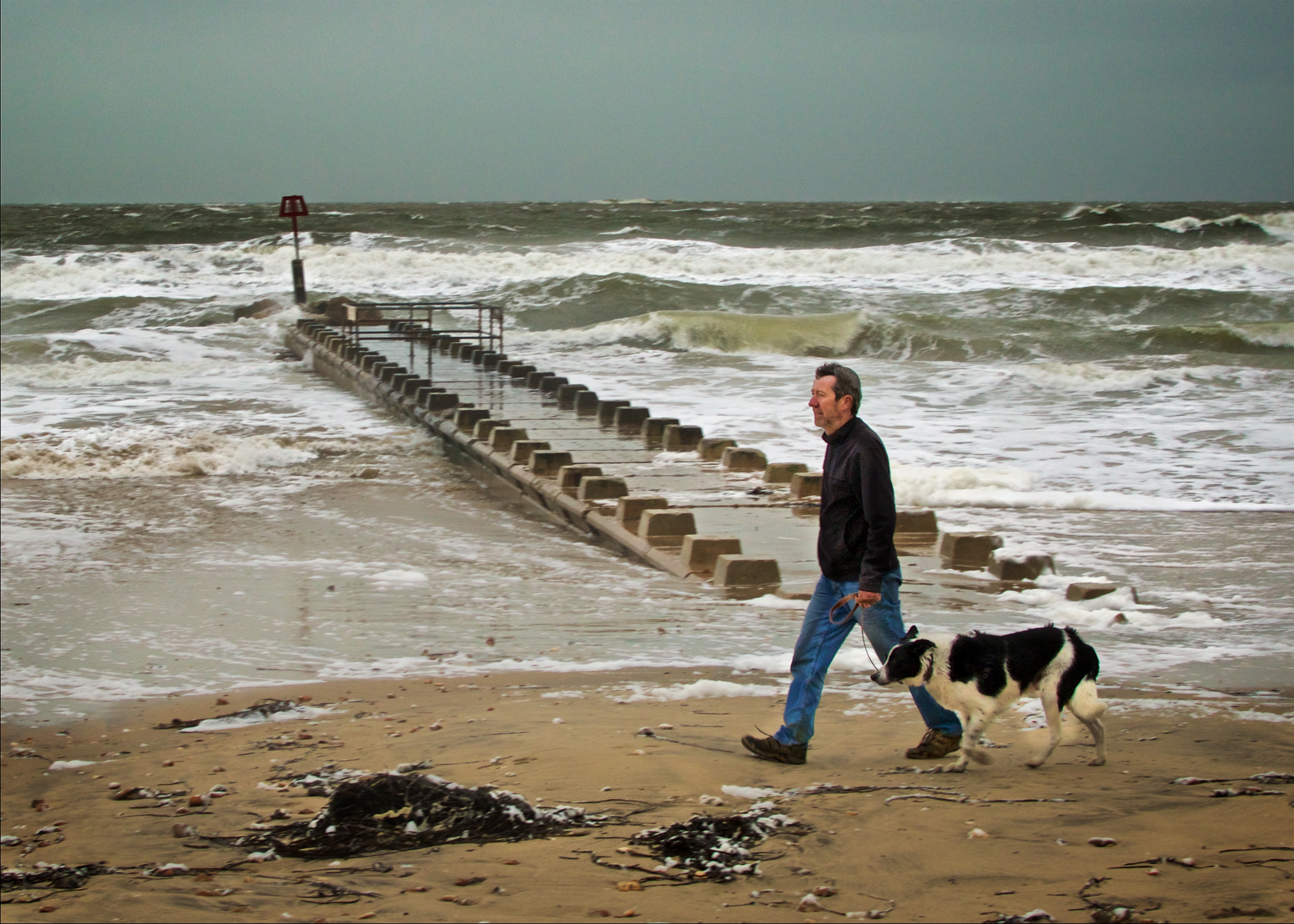 A man takes his dog on their morning constitutional, despite it being Christmas Day and very stormy at Bournemouth Beach